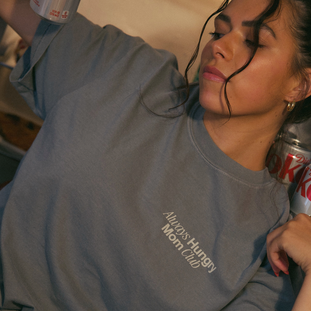 [main] A mom wearing a grey T-shirt with the phrase "always hungry mom club" on the front of the shirt. 